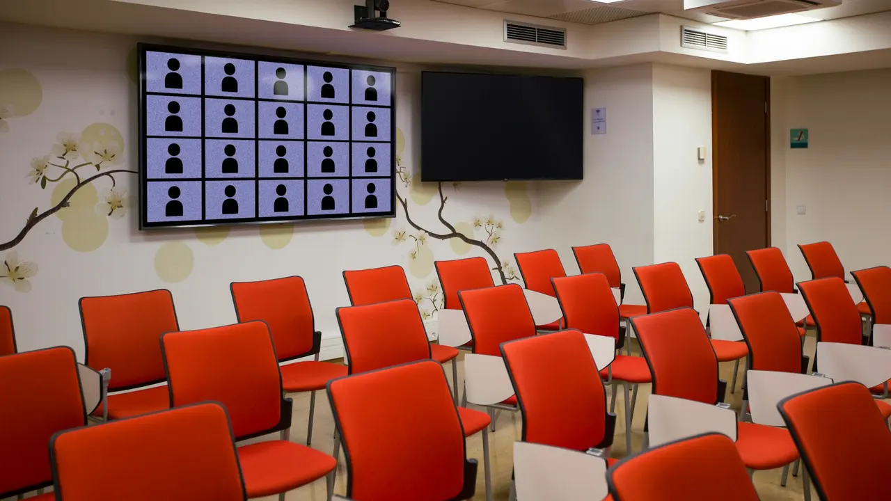 Kırmızı sandalyeli bir seminer salonunda duvara asılı büyük dijital ekran